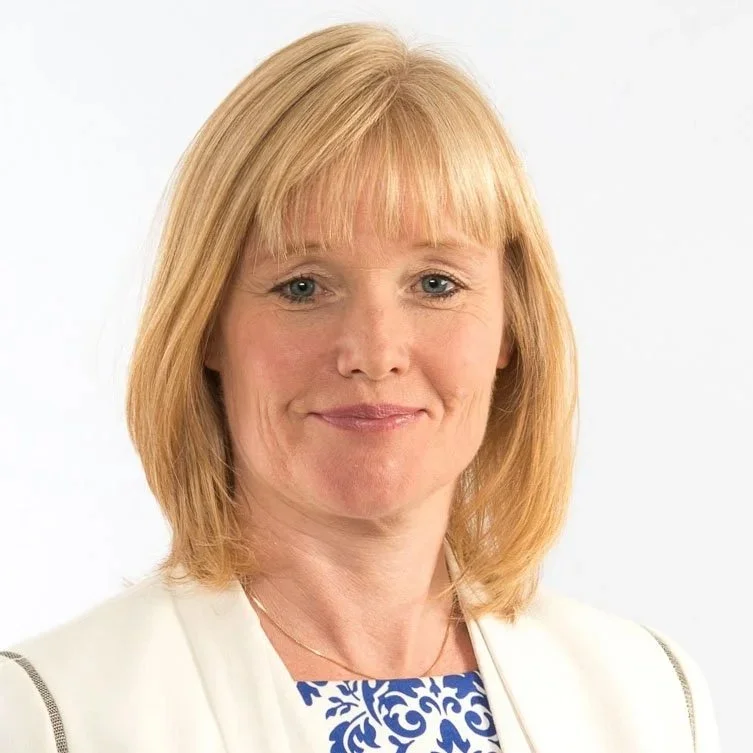 A woman, Alvhild Hedstein, with blonde hair smiling, wearing a white blazer and a blue patterned top against a plain white background.