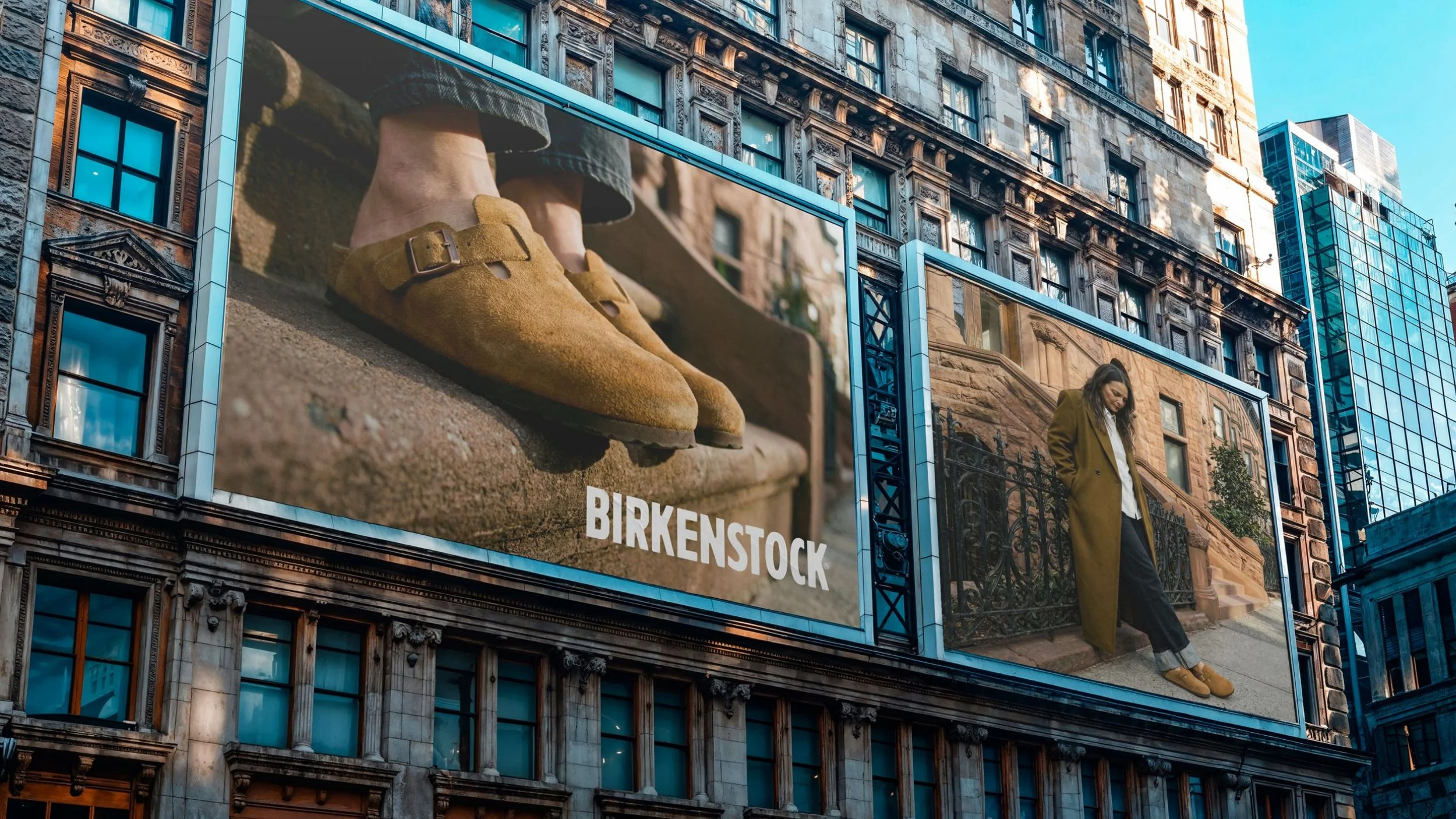 Zwei große Werbetafeln an einem Stadthaus, eine zeigt eine Nahaufnahme von braunen Schnürschuhen, die andere eine Frau in einem Mantel auf der Straße, darüber befindet sich das Wort 'BIRKENSTOCK'.