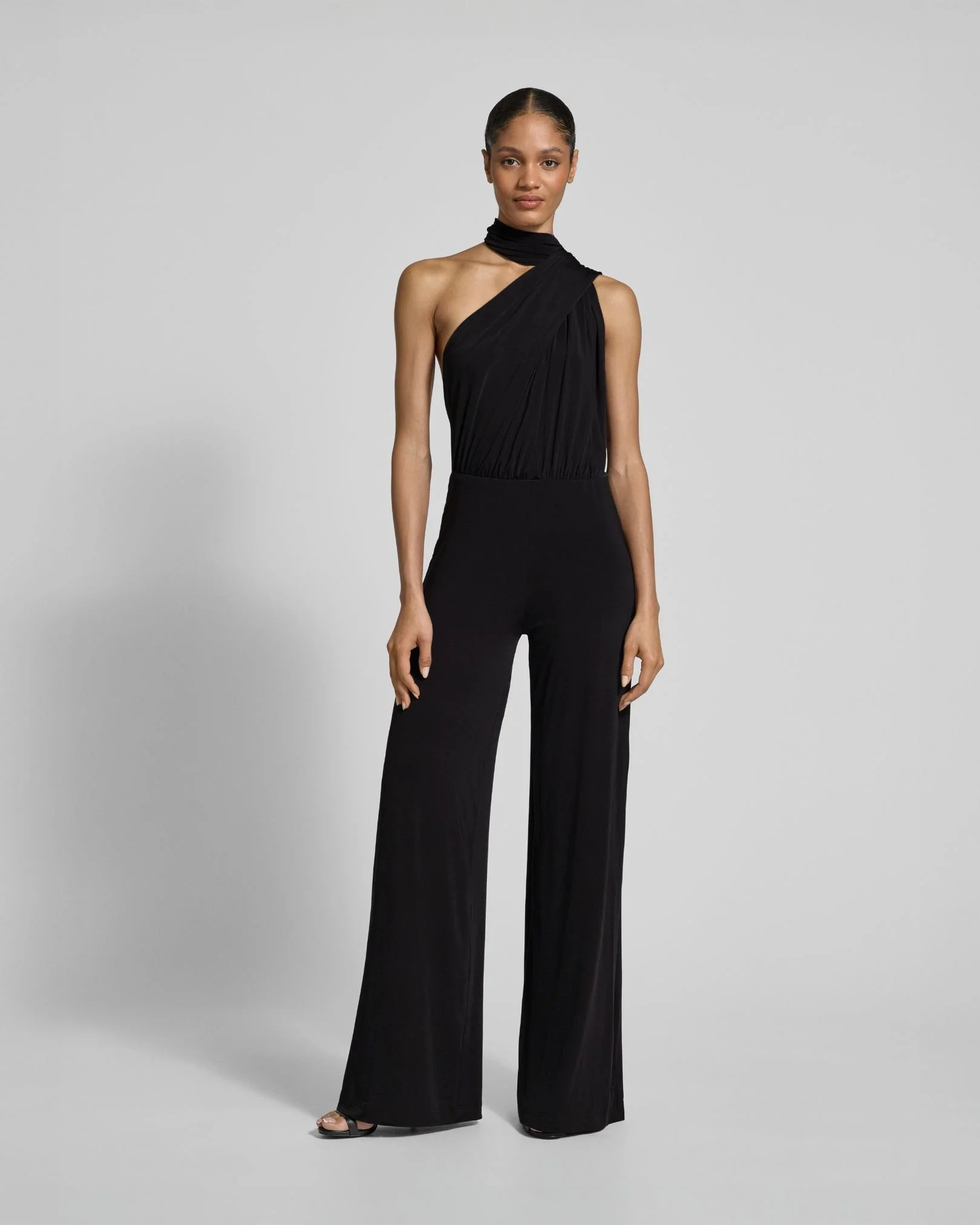 Frau in schwarzem eleganten Outfit mit weiten Hosen und einem asymmetrischen Oberteil, das über einer Schulter getragen wird.