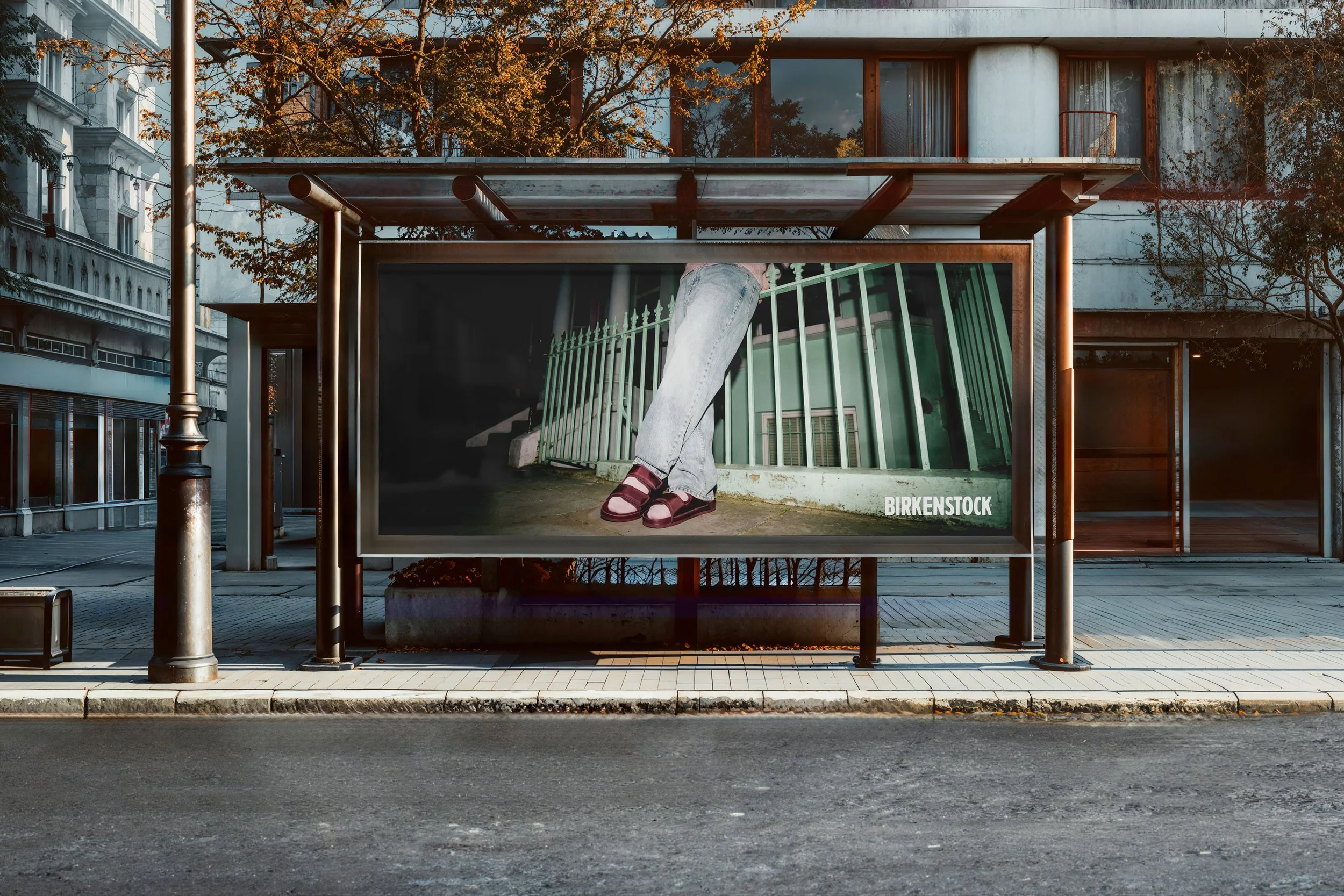 Werbetafel an einer Bushaltestelle mit einem plakatierten Bild eines Beines mit Sandalen und Jeans, davor ein Zaun und eine grüne Fassade.