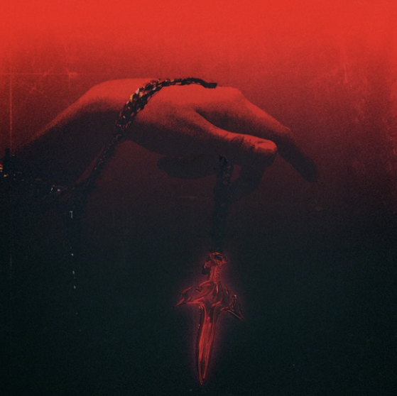 A hand holding a pendant with a shark fin design, illuminated by red and dark lighting.