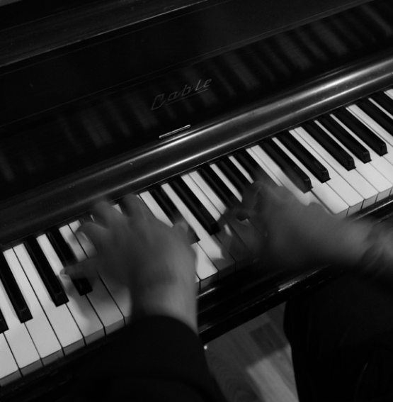 Hands playing a black grand piano keyboard in black and white