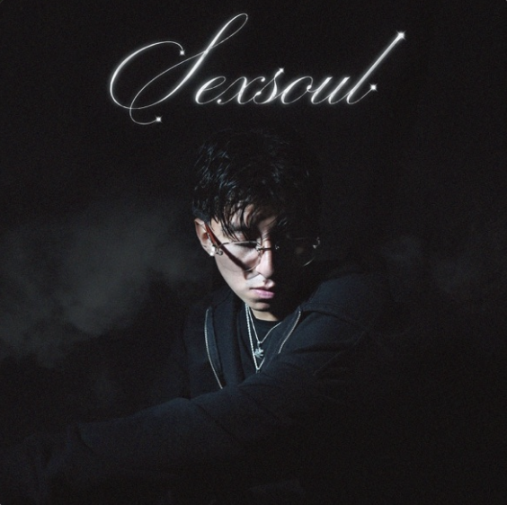 A dark image with the word "Sexpout" written in glowing cursive at the top. A person with dark hair, glasses, and jewelry is in the lower part of the image, looking down.