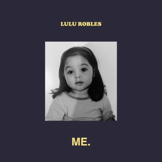 Black and white photo of a young girl with long hair, wearing a light-colored shirt with a darker collar, set against a dark background with the name "Lulu Robles" above and the word "Me" below.