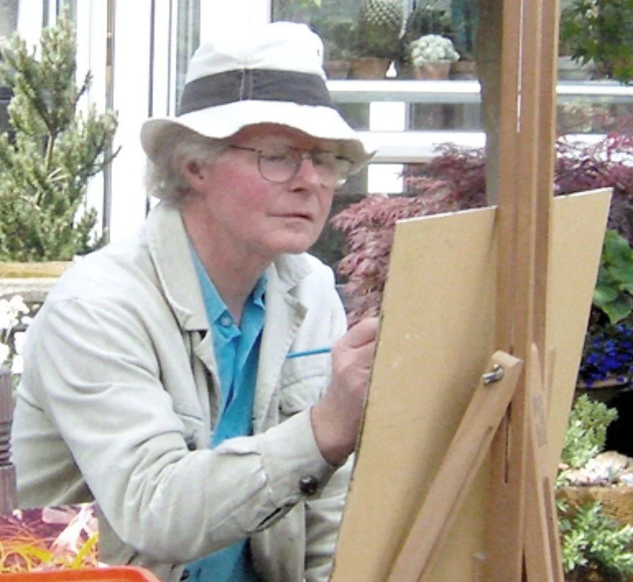 An older man painting at an easel outdoors, wearing a white hat and glasses, surrounded by plants.