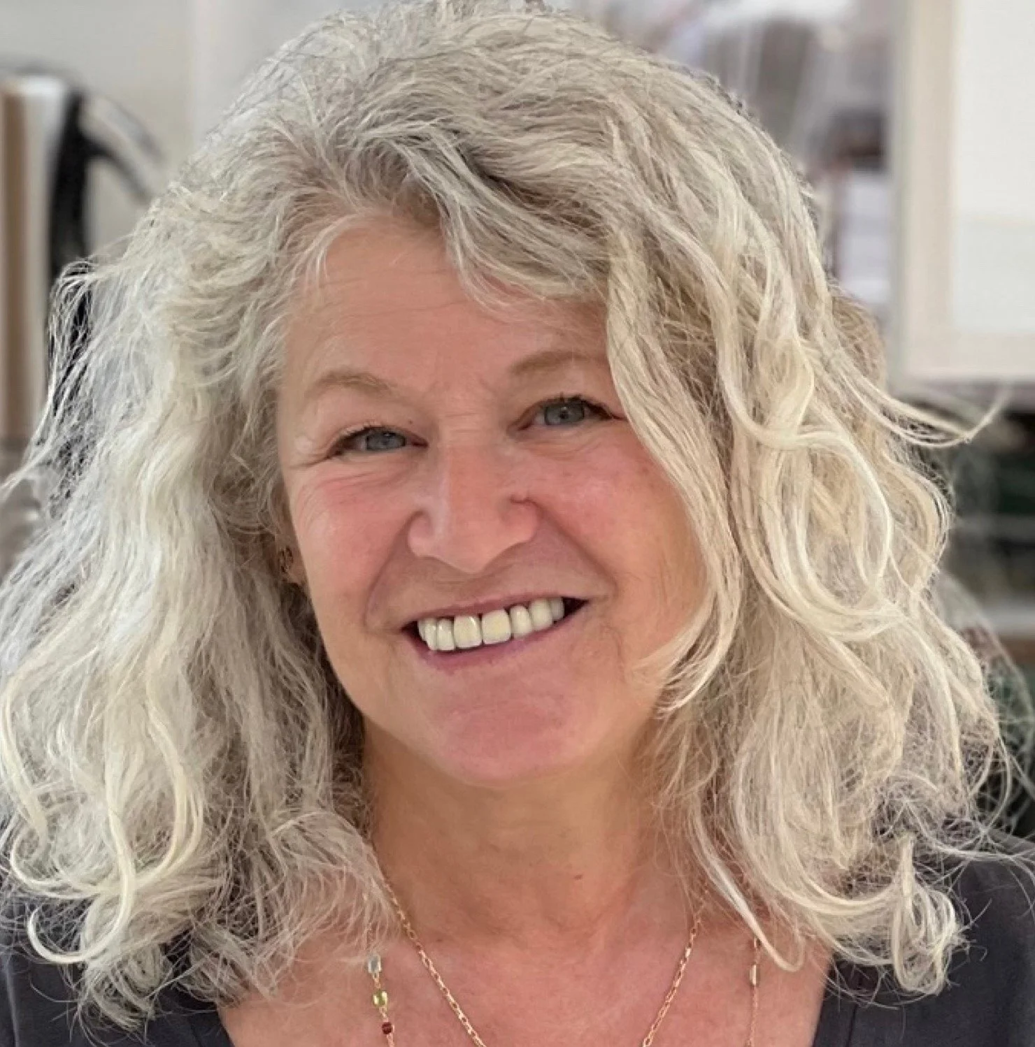 Smiling person with curly gray hair indoors.