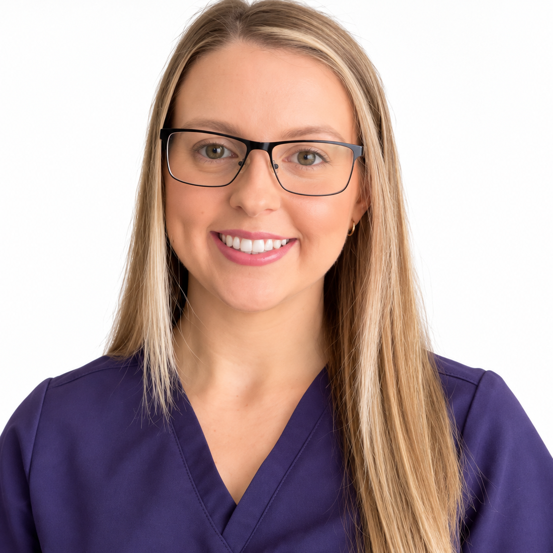 A woman with long blonde hair, wearing glasses and a navy medical uniform. She is smiling and standing against a plain light-colored wall.