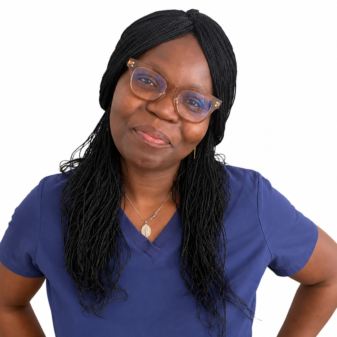 A woman with black braids wearing glasses, a blue shirt, a necklace, a watch, and a ring, standing against a beige wall.