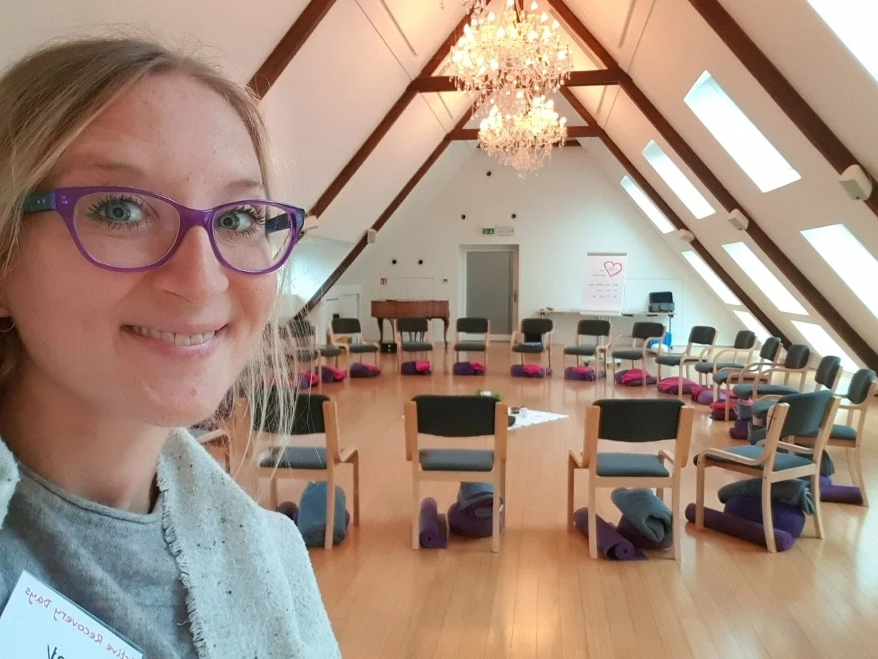 Ein Raum mit Stühlen und Yogamatten, vorbereitet für eine Aktivität wie Yoga oder Meditation, mit einem Kronleuchter und Dachfenstern in einem Raum mit schrägen Decken.