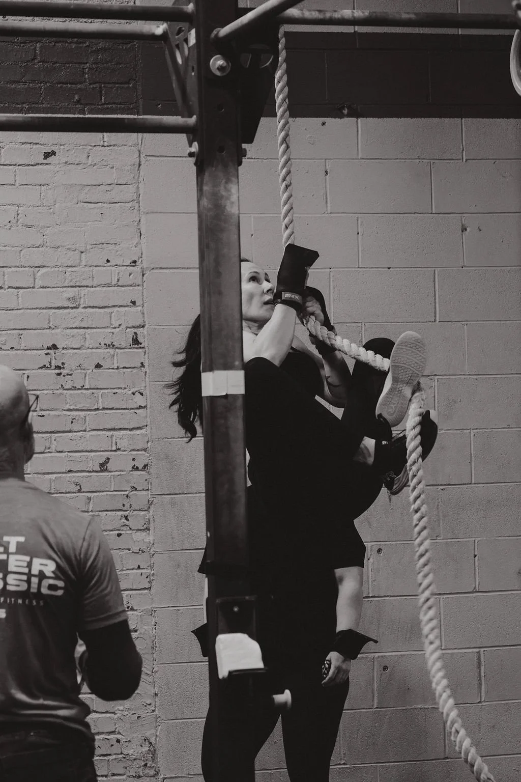 Woman climbing rope during a workout in a gym.