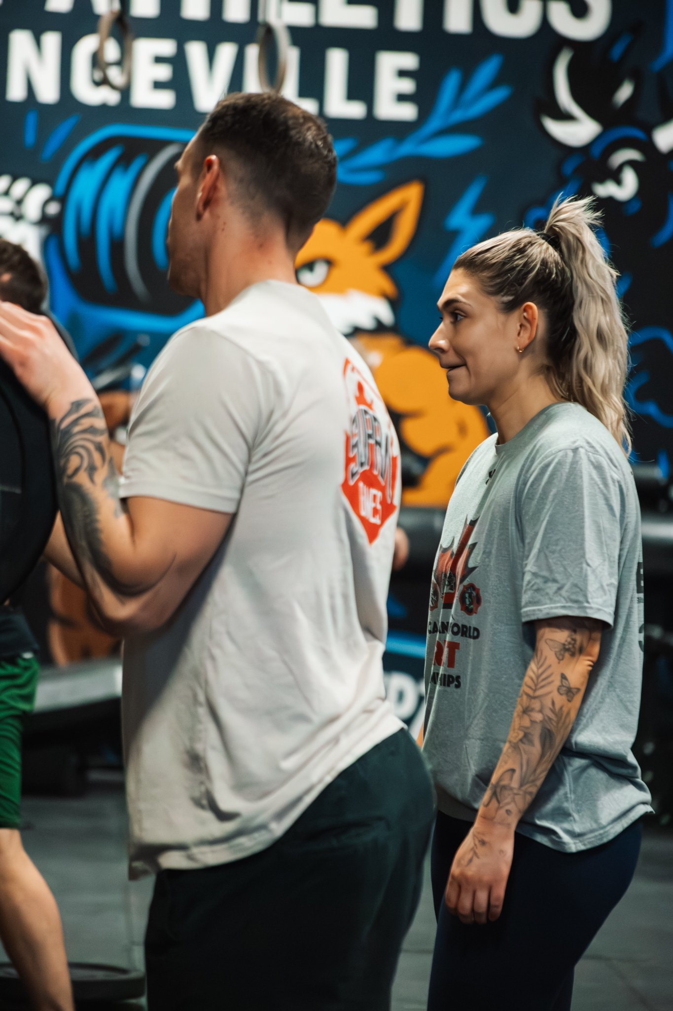 People training at CrossFit gym with a colorful mural of a fox and a camera in the background.