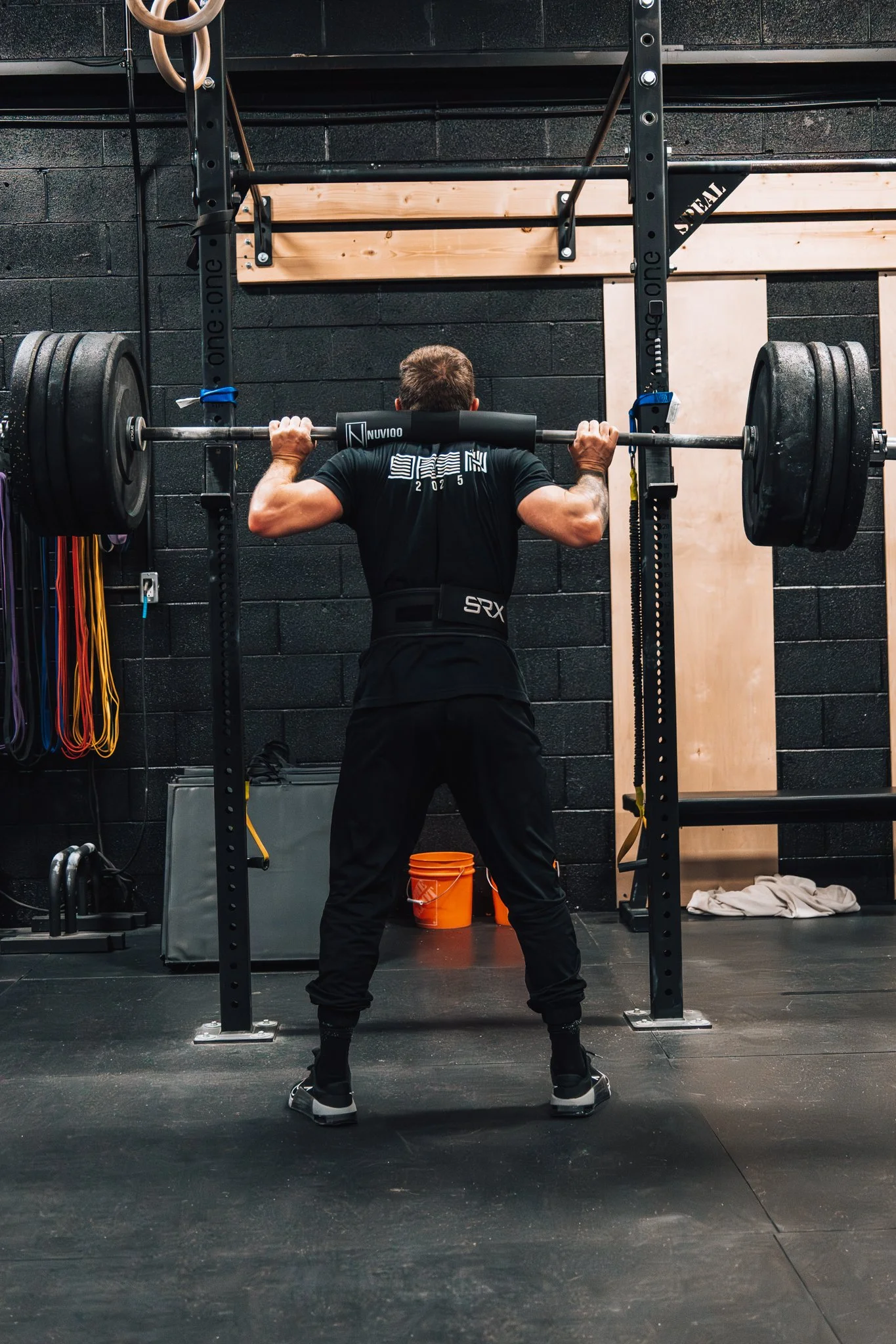 Man lifting weights in a gym, squatting with a barbell loaded with weights on his shoulders.