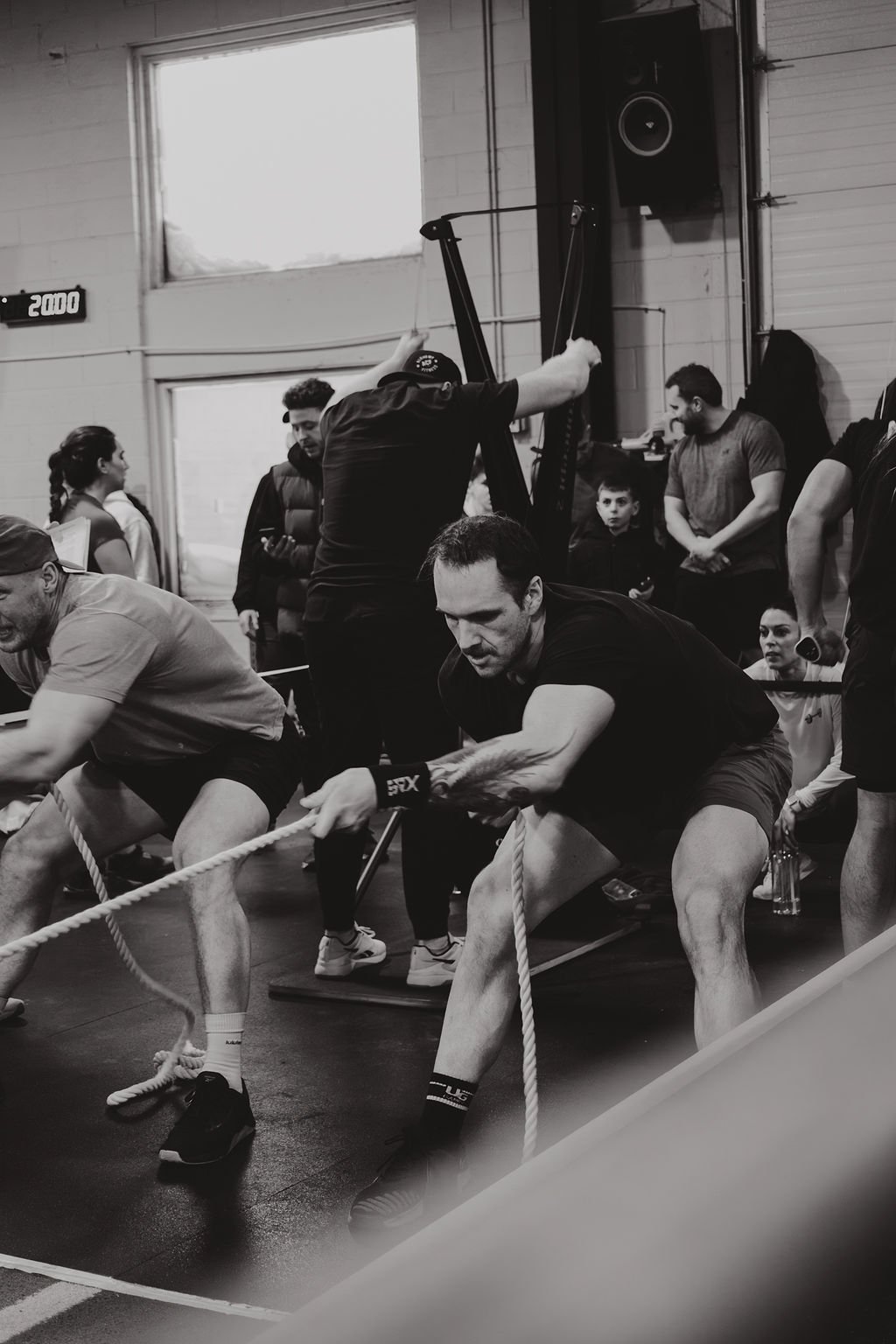 People participating in a tug-of-war competition indoors, pulling on a rope, with others watching in the background.