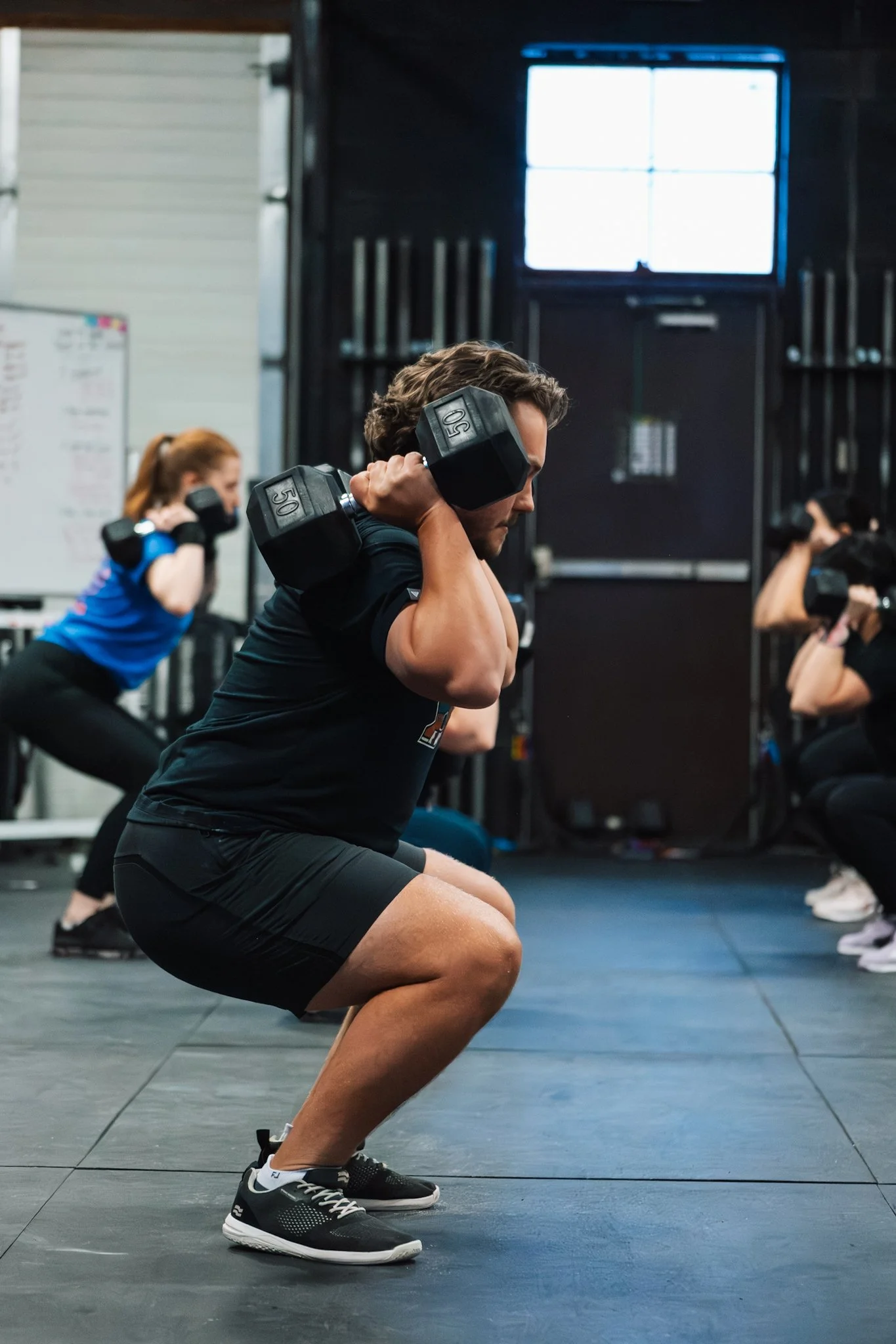 People working out with dumbbells during a squat exercise in a gym.