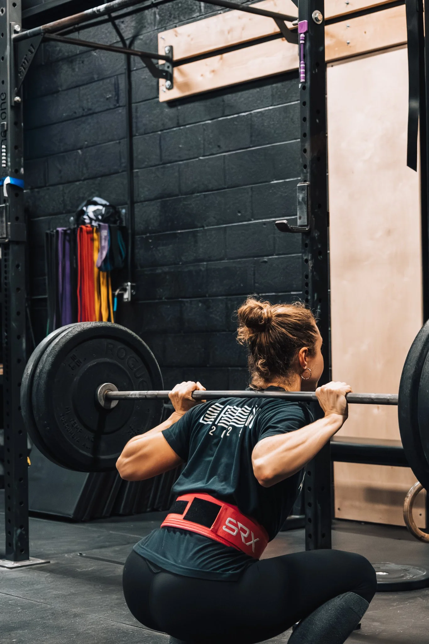 Woman performing squat exercise with barbell in gym.