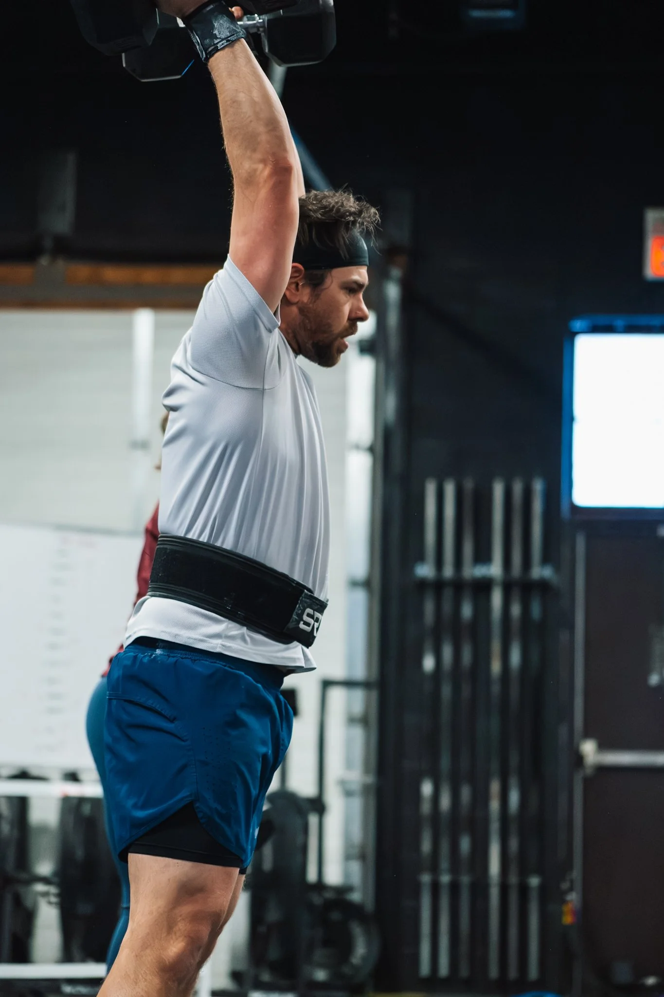A man lifting a dumbbell overhead during a workout at a gym.
