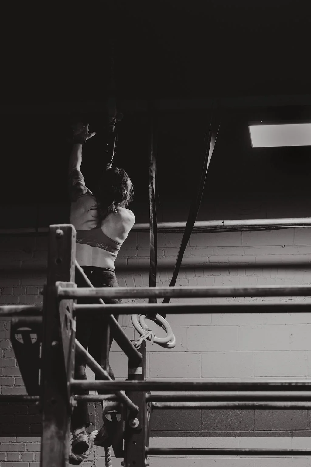A woman in sports bra and pants climbing gymnastics rings in gym.