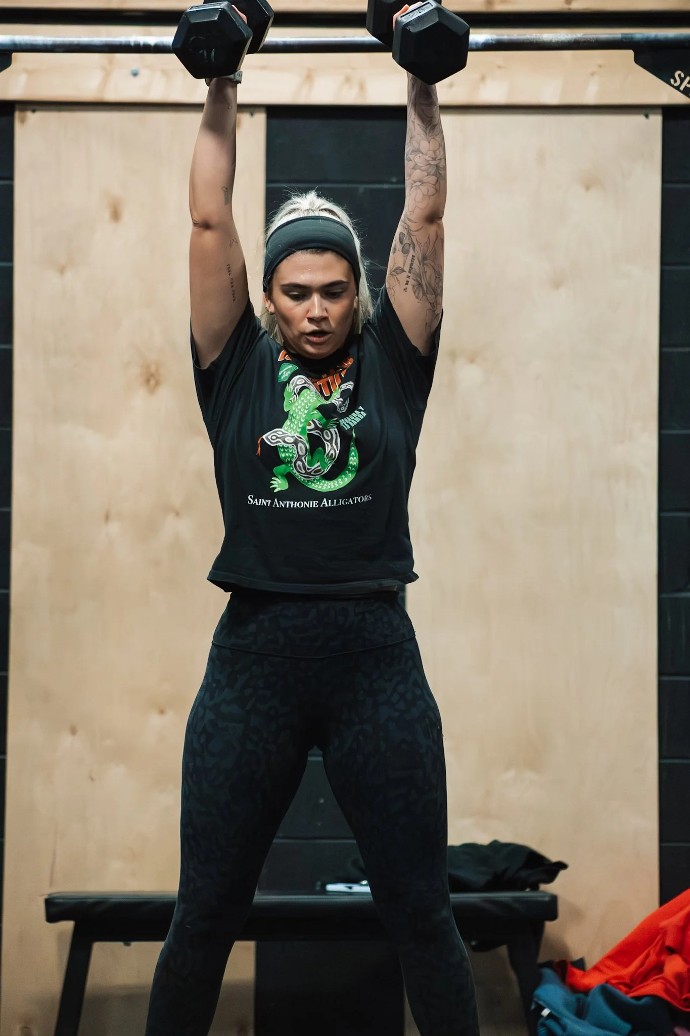 A woman lifting a dumbbell overhead during a workout at a gym.