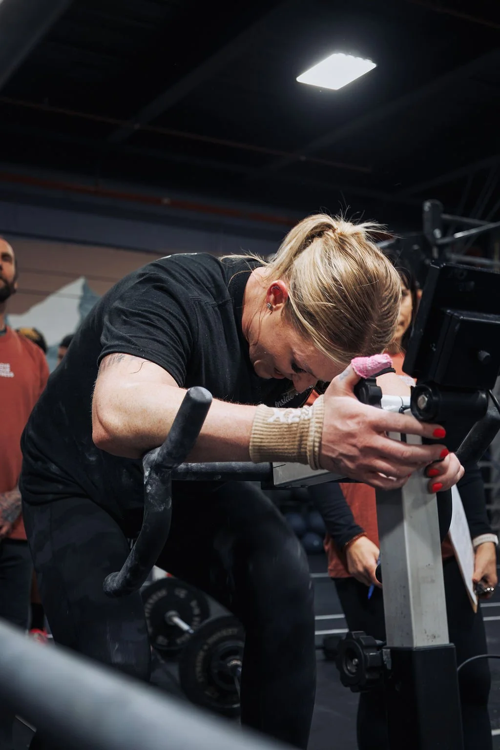 Woman intensely focused on a rowing machine in a gym, with others around her.