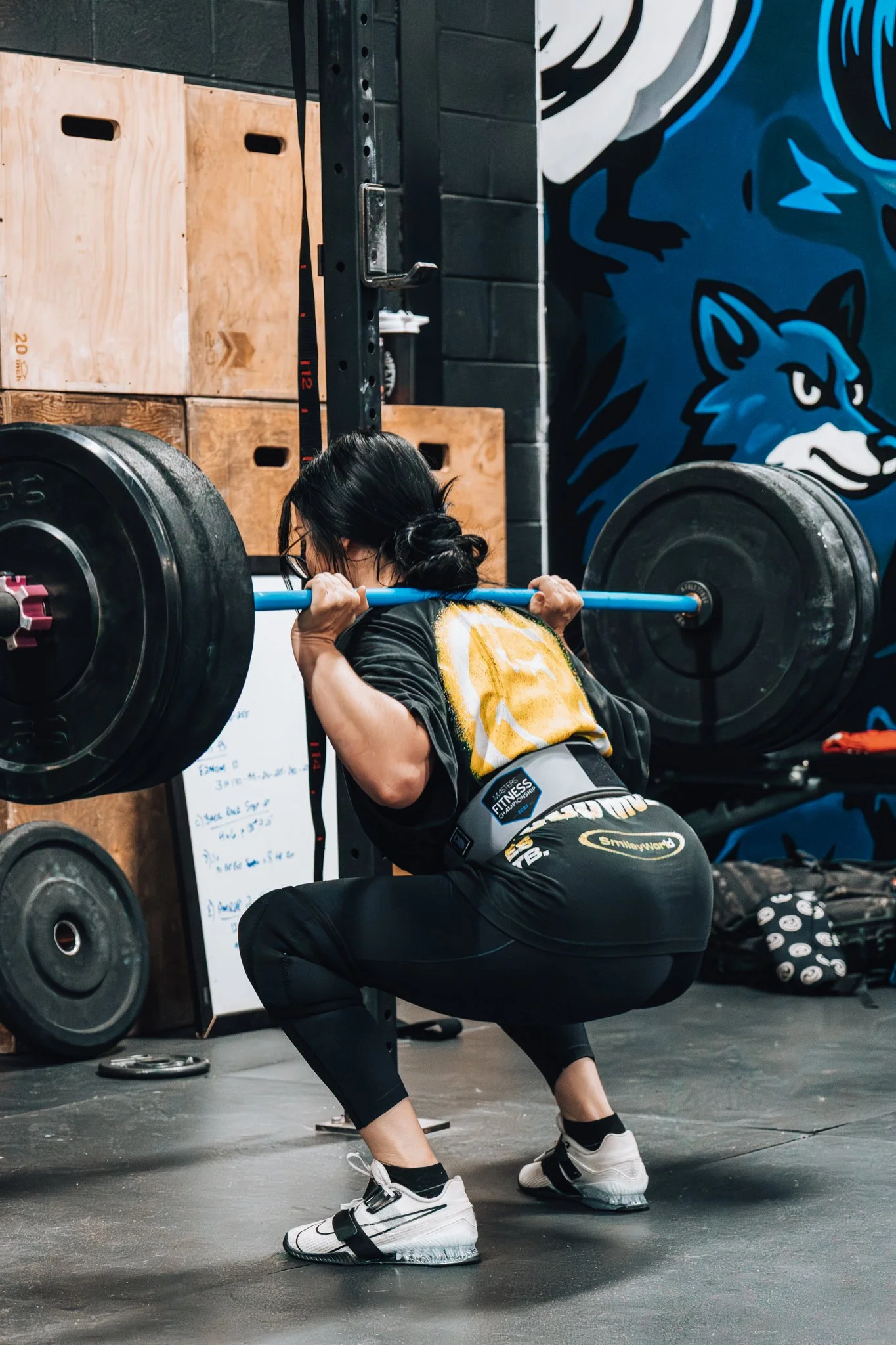 A woman is performing a squat exercise with a loaded barbell on her shoulders in a gym.