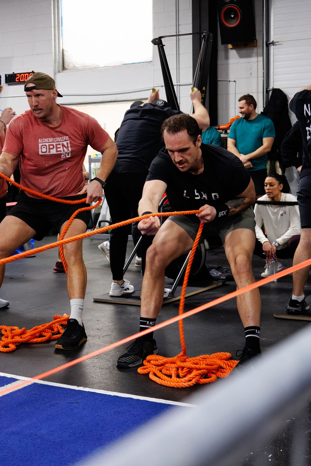 People participating in a crossfit competition, pulling orange ropes in a gym.