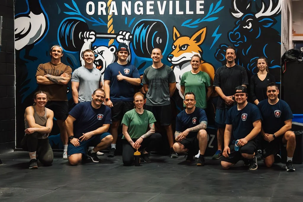 Group of people posing in front of a mural with animals and the text 'Orangeville'.
