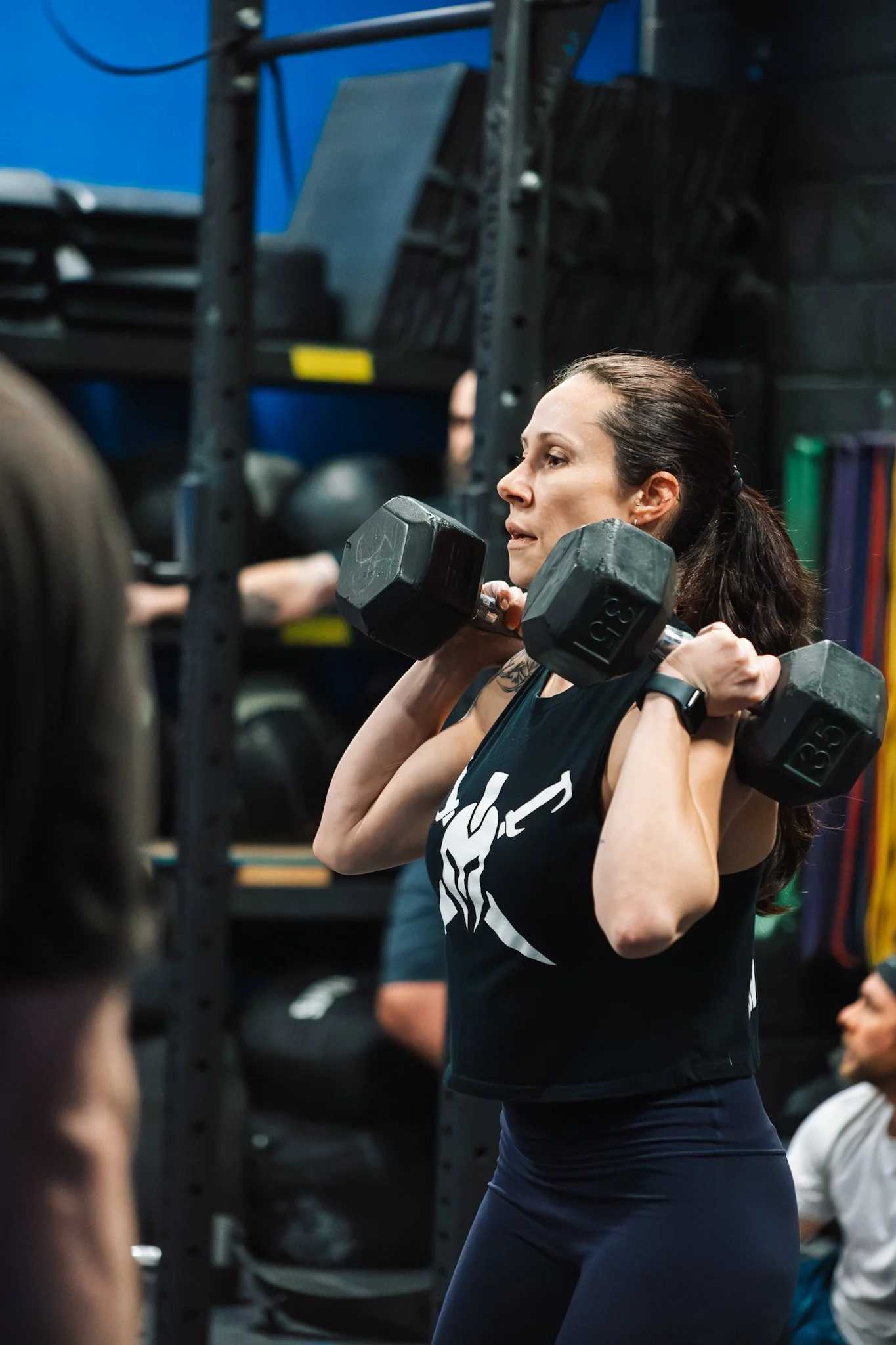Woman lifting a dumbbell at the gym, surrounded by gym equipment and other people.