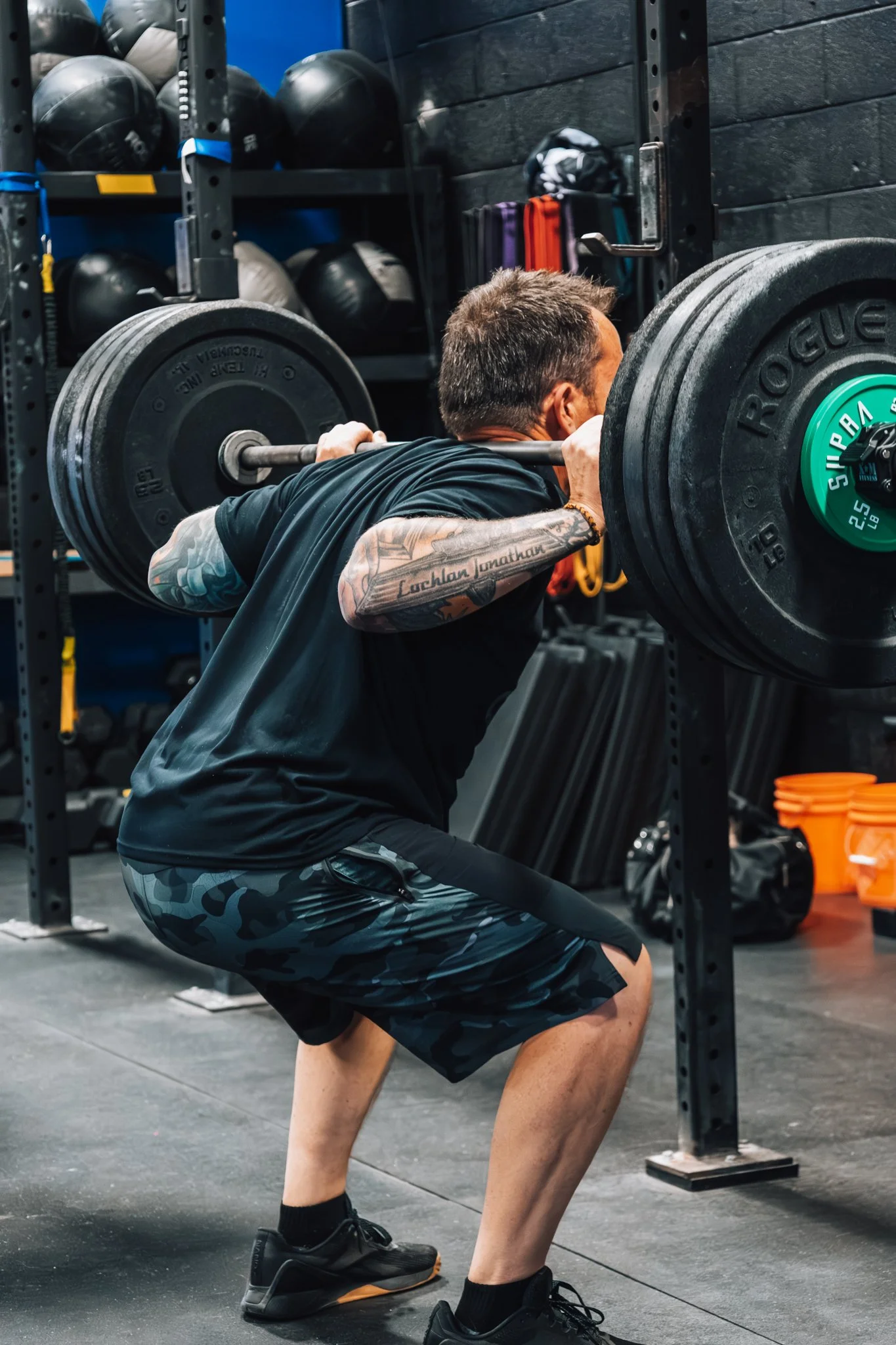 A man performing a squat exercise with a barbell loaded with weight plates in a gym.