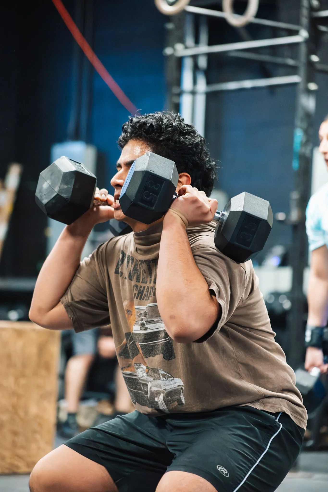 Young man doing a squat exercise with dumbbells across his shoulders in a gym.