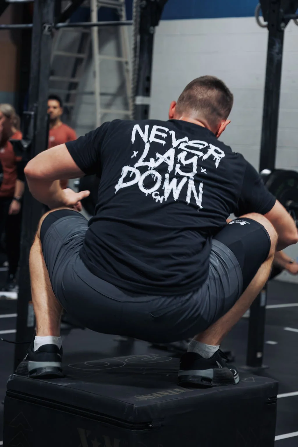 Man squatting on a plyometric box during a workout at a gym.