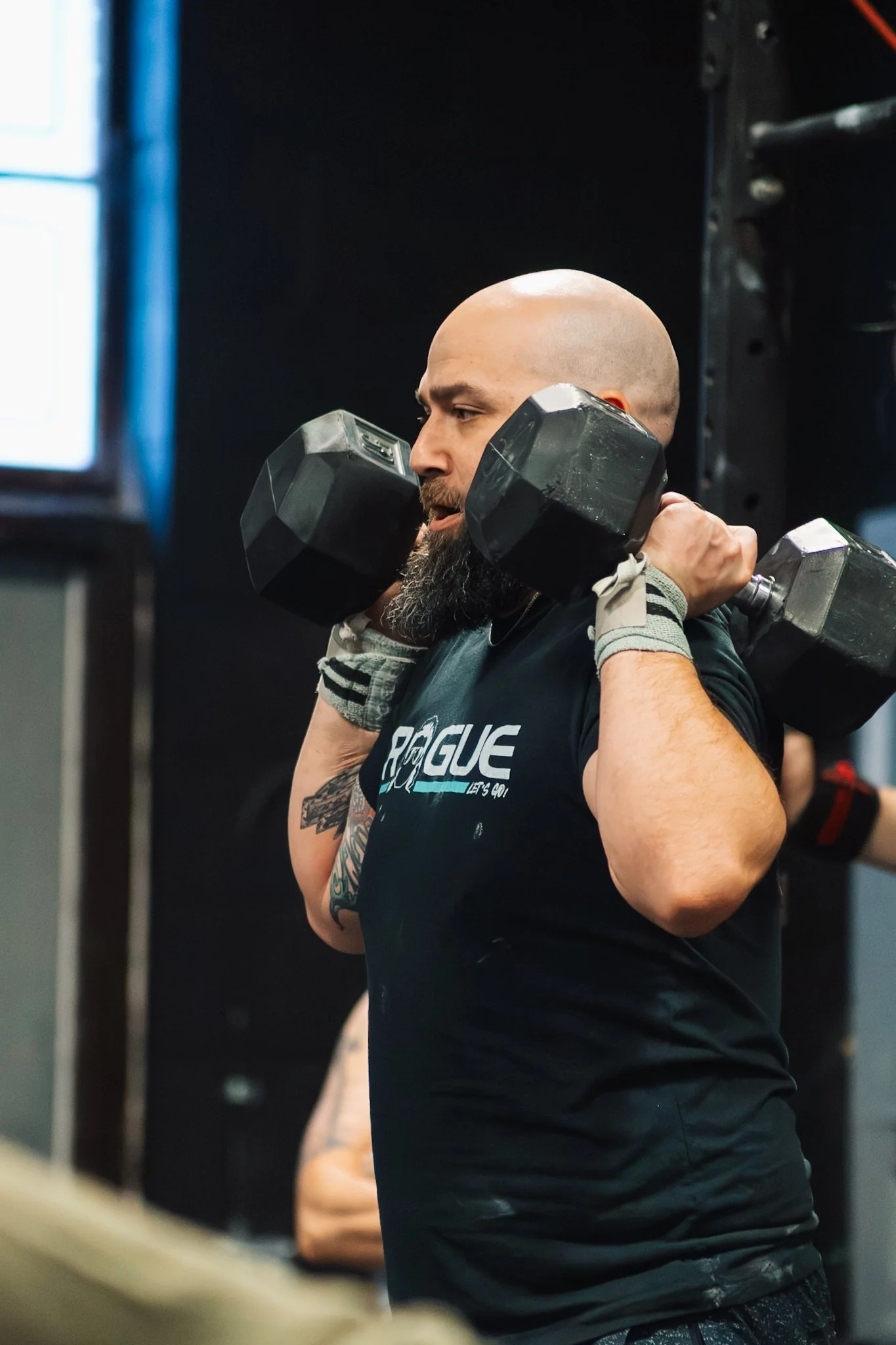 Man lifting two dumbbells on his shoulders during exercise at gym