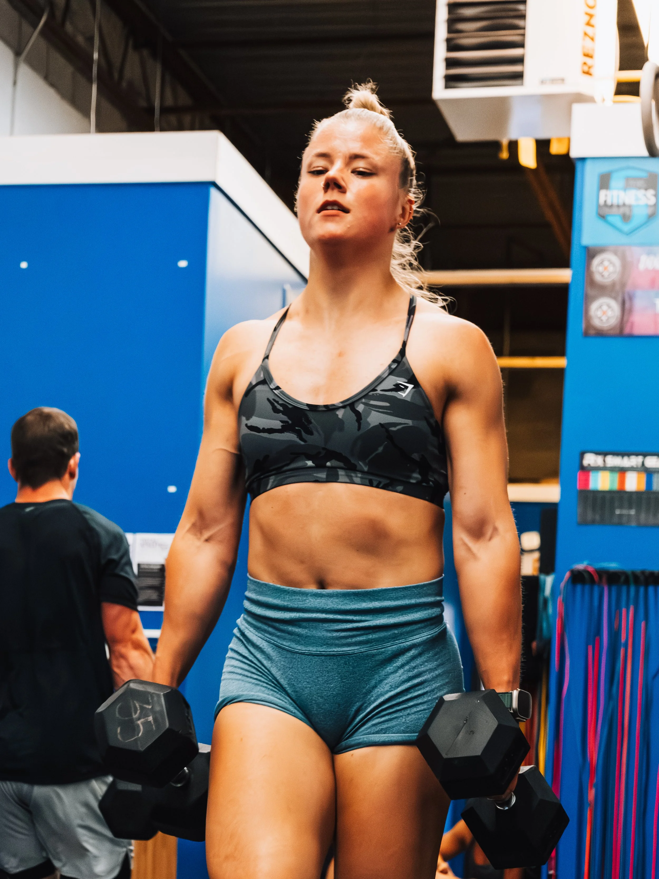 A woman in workout attire lifting dumbbells in a gym.