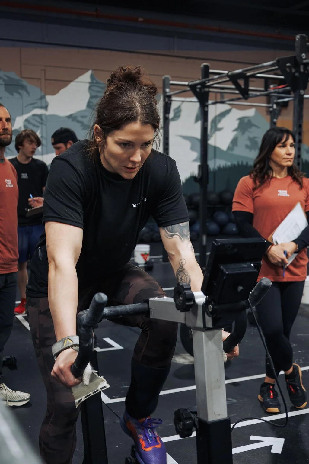 Woman working out on a rowing machine in a gym with other people in the background.