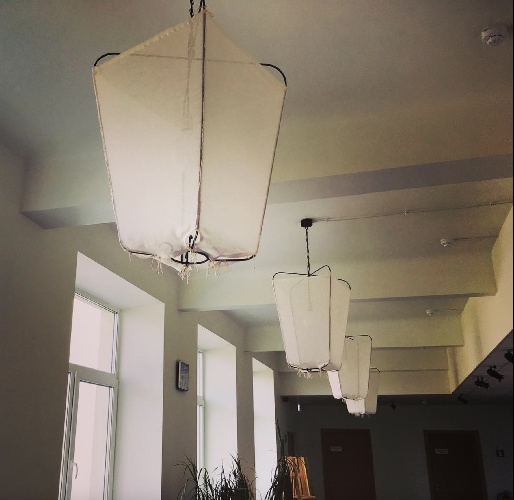Multiple rectangular white fabric lanterns hanging from the ceiling in a room with large windows and white walls.
www.gardenlampcollection.com