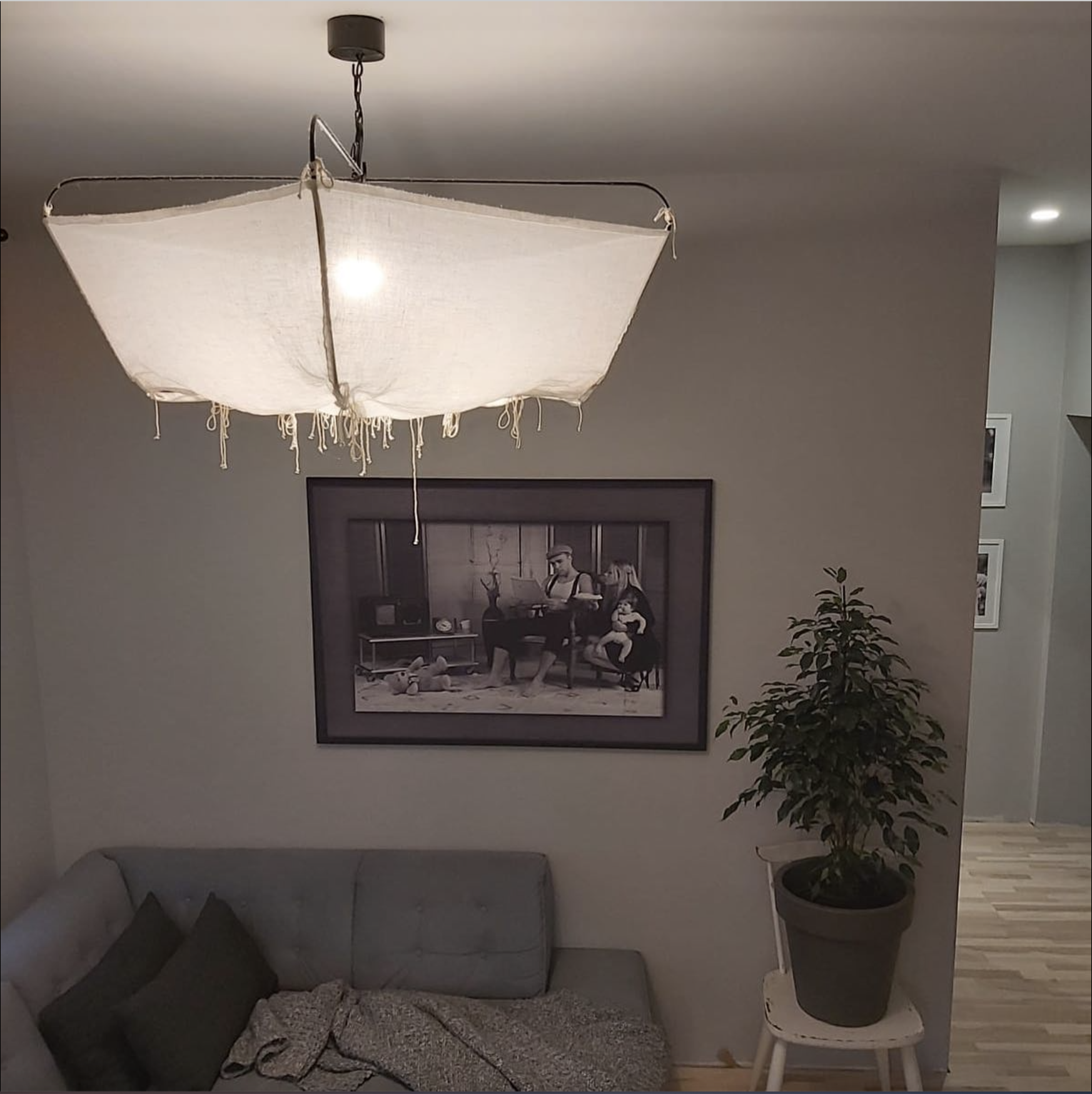 Living room with a gray sofa, a large wall art picture, a potted plant on a white stool, and a distinctive paper lampshade hanging from the ceiling.
www.gardenlampcollection.com