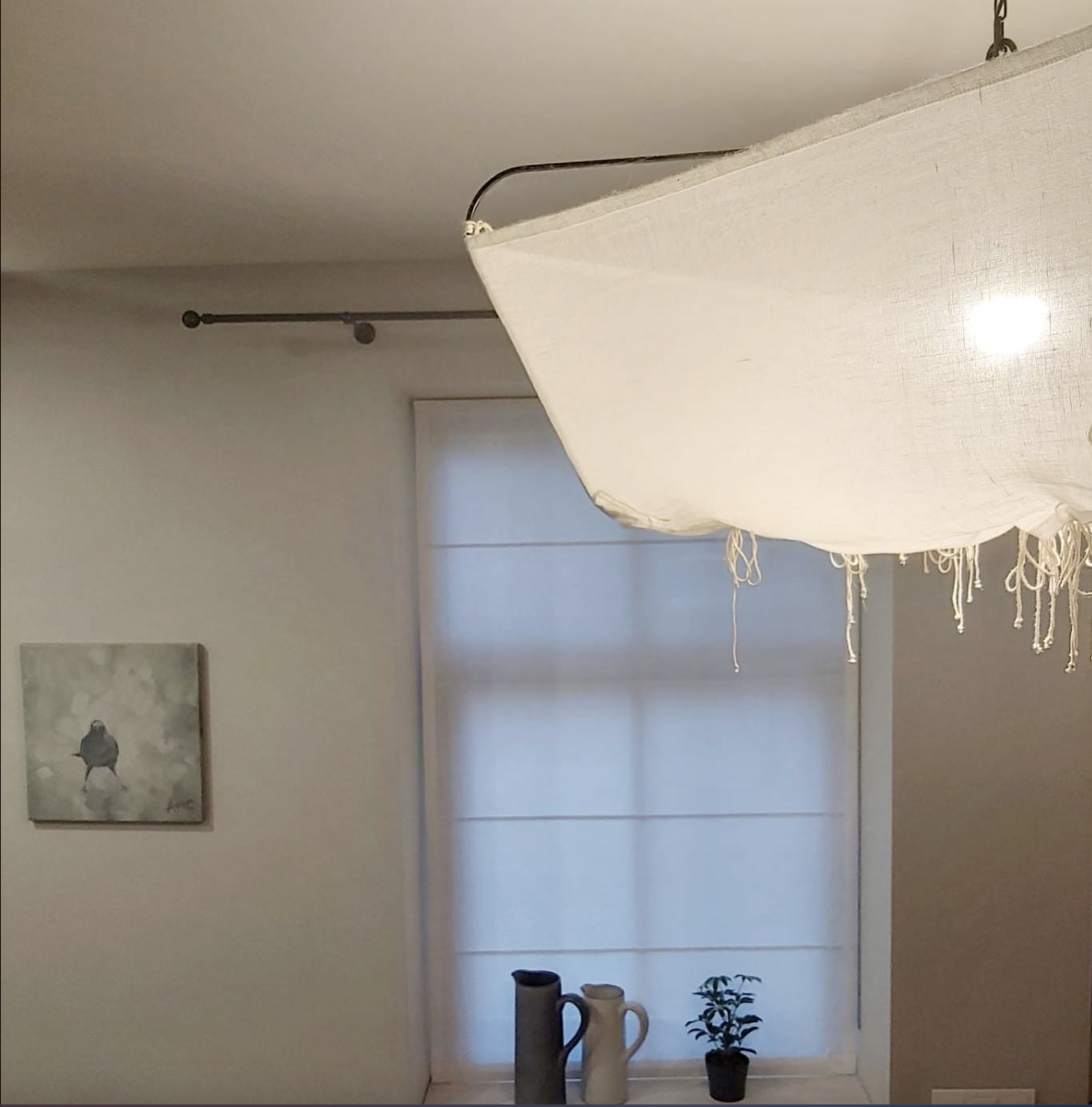 Interior room with a window covered by a white shade, a hanging white fabric pendant light, a small potted plant, and two ceramic pitchers on the windowsill.
www.gardenlampcollection.com