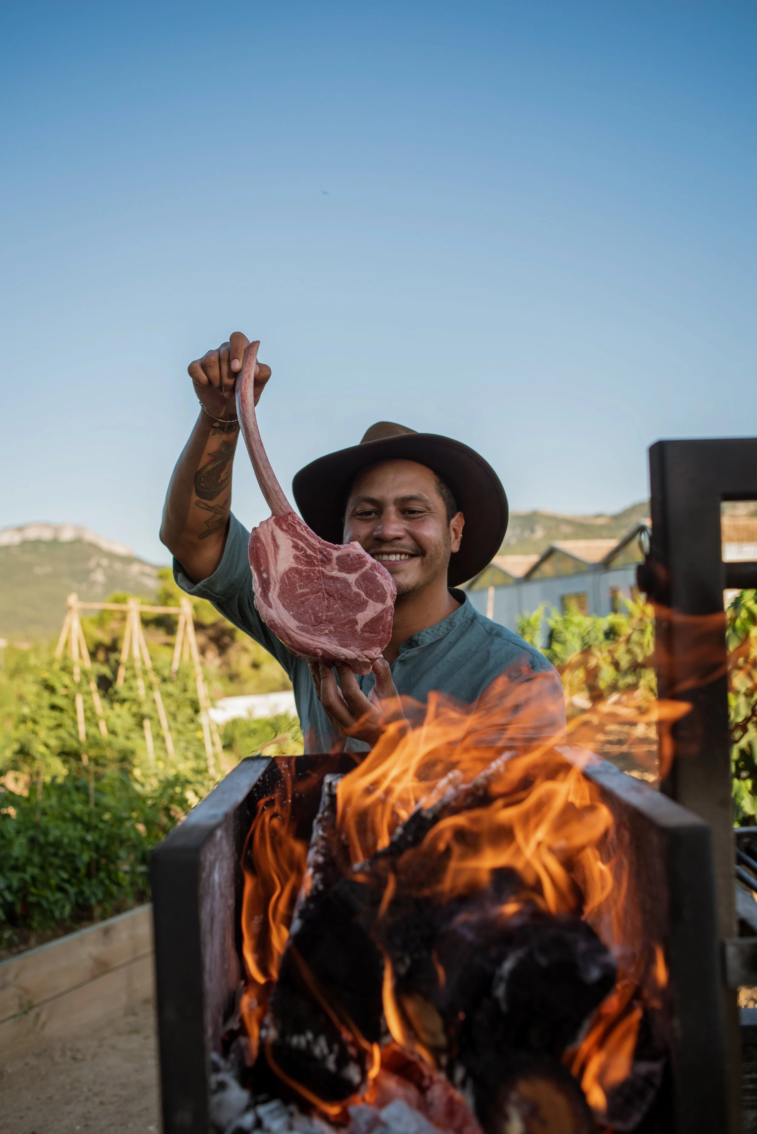 Persona sosteniendo un gran corte de carne cerca de una parrilla con fuego.