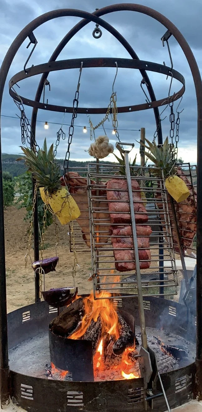 Personas reunidas alrededor de una parrilla en un espacio al aire libre, con botellas de champán en primer plano.