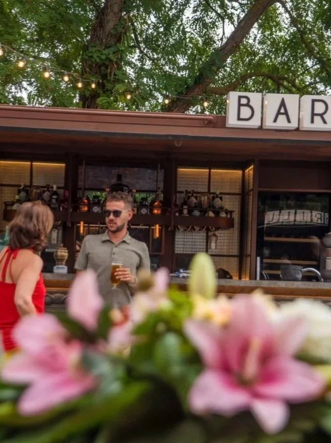 Grupo de personas en un evento social al aire libre frente a un edificio de estilo colonial con jardines y decoración luminosa.