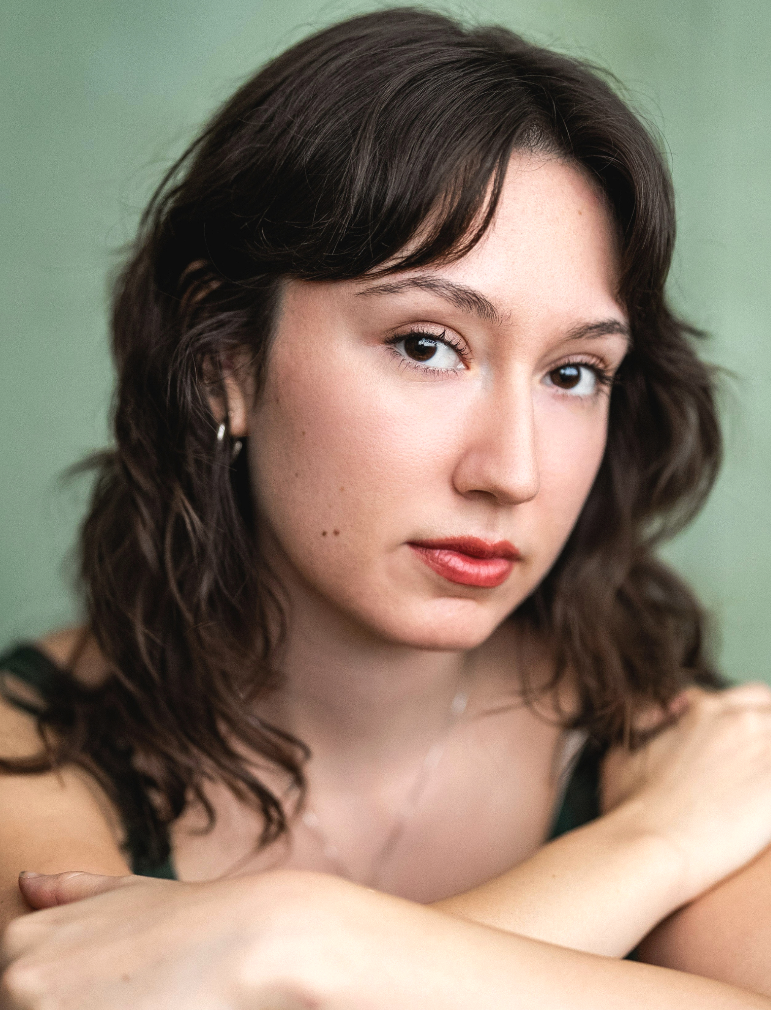 Close-up of a young woman with wavy brown hair and light skin, looking at the camera, with a green background.