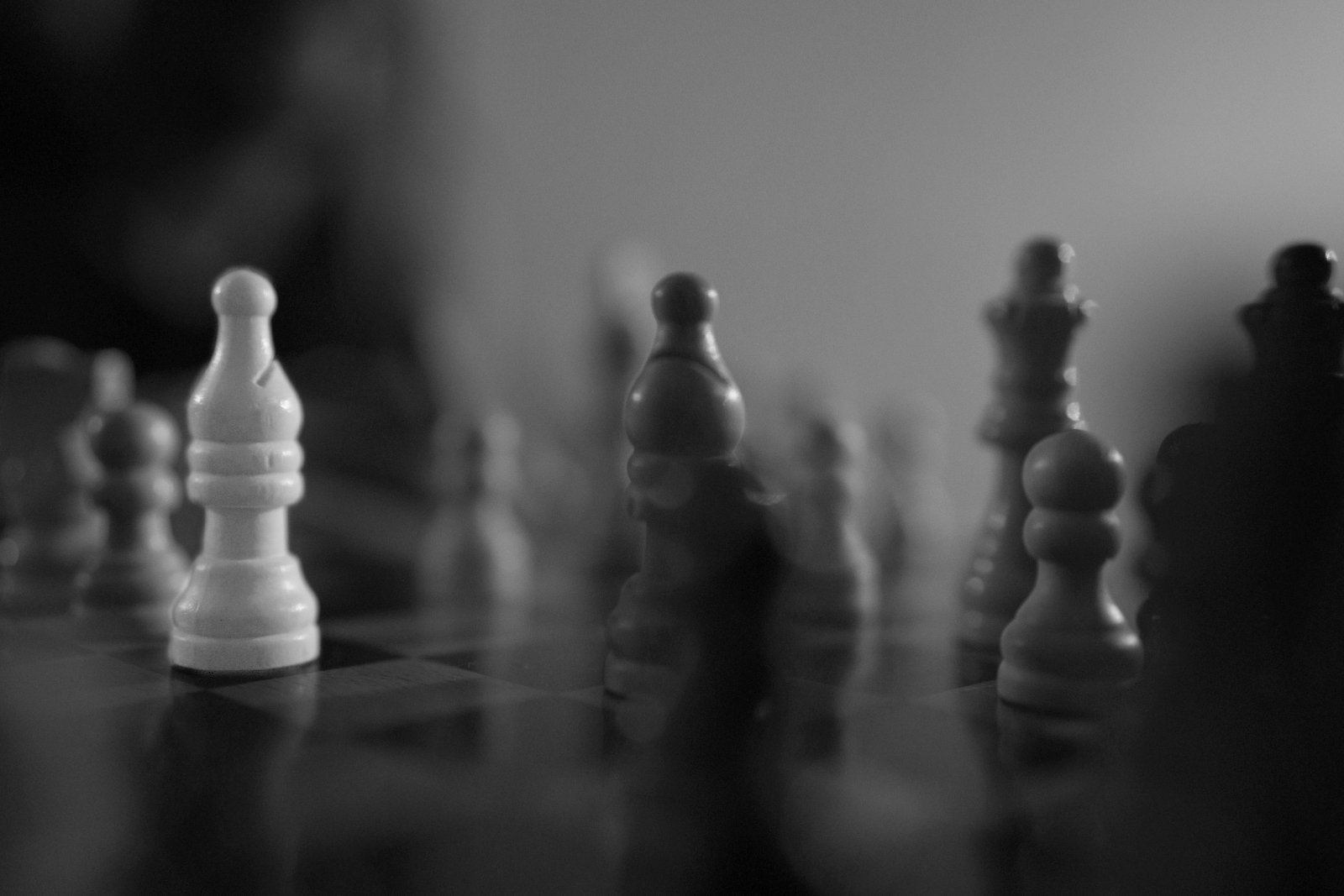 Black and white close-up of chess pieces on a chessboard, with some pieces in focus and others blurred in the background.