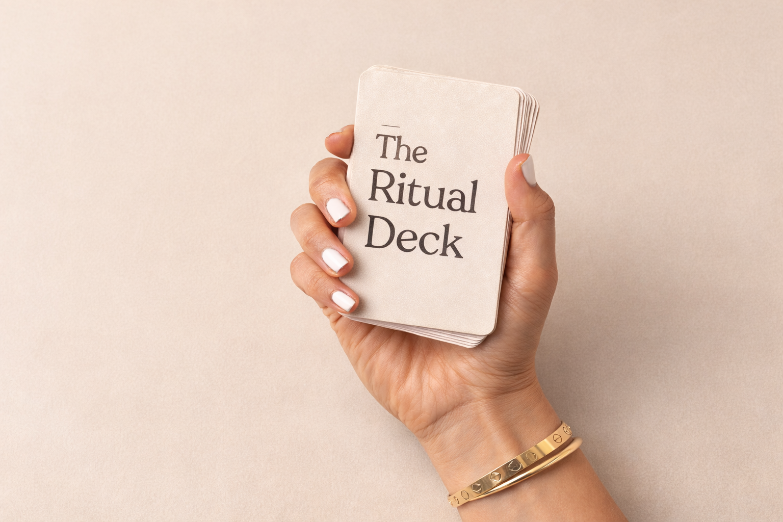 A person's hand holding a small deck of cards with the words 'The Ritual Deck' printed on the front, against a beige background.