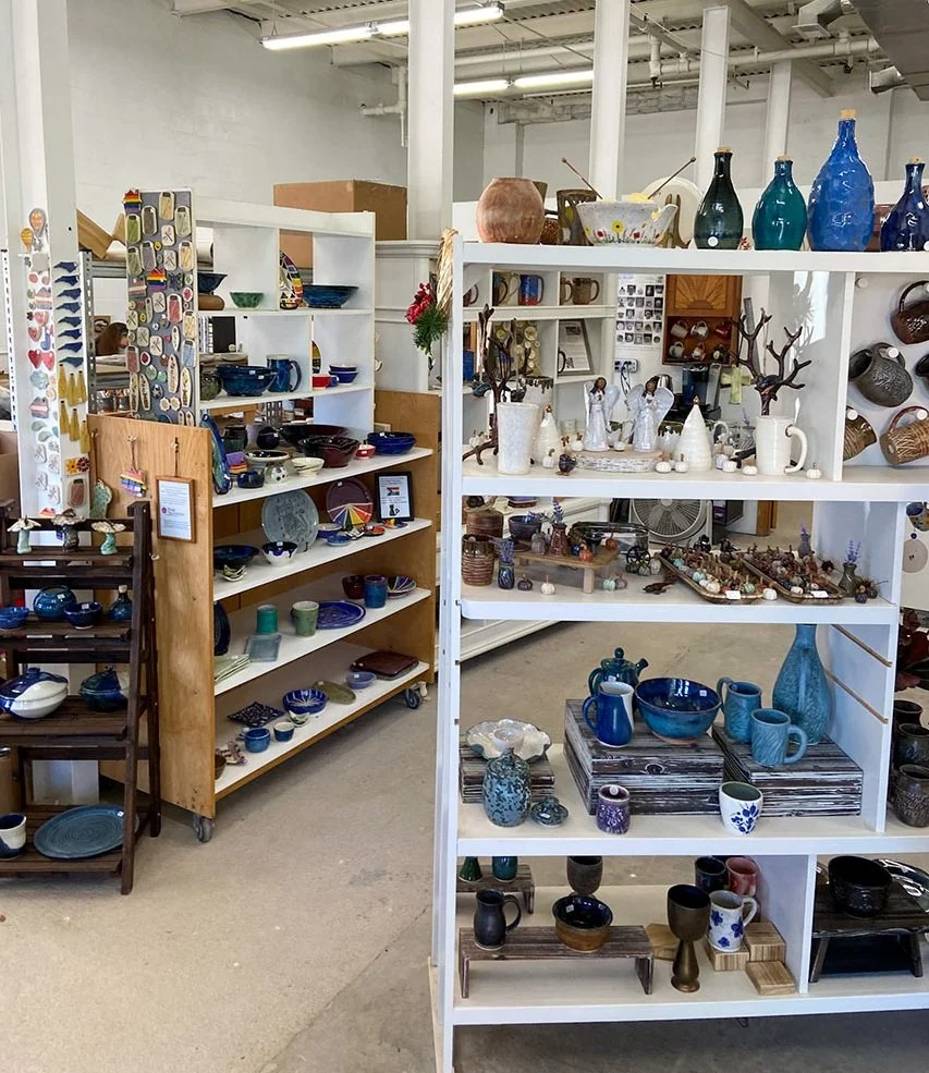 Display of various pottery and ceramic items in our gallery , including vases, bowls, and decorative pieces on white and wooden shelves.