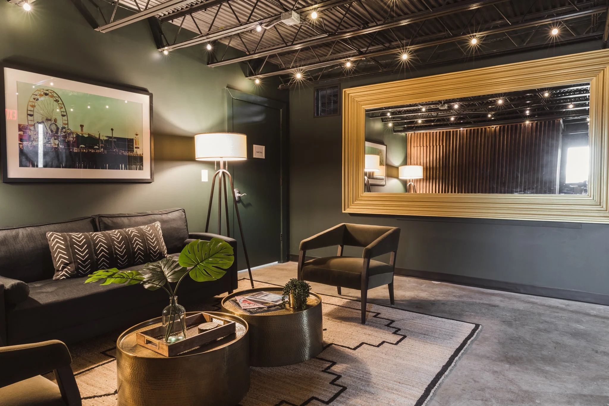 Seating area with a dark sofa, brass coffee tables, a geometric rug and an oversized gold mirror