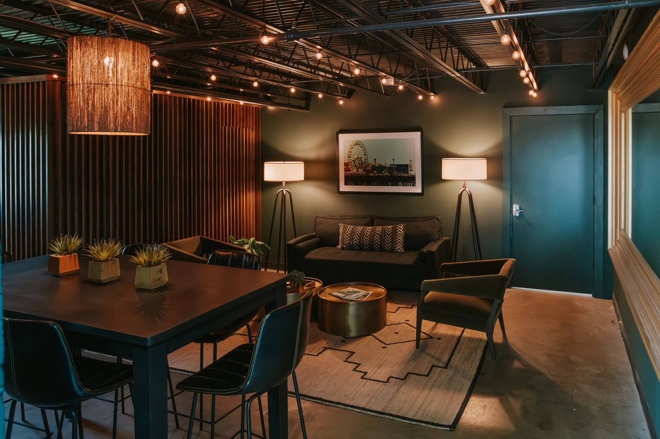Green Room with dark green walls, a pub table, rattan pendant light, leather sofa and tripod floor lamps