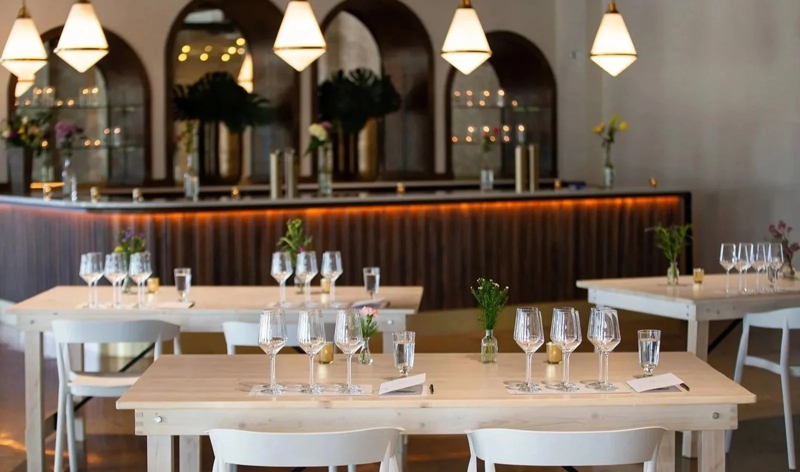 Tasting setup with light wood tables, wine glasses and bud vases in front of the bar