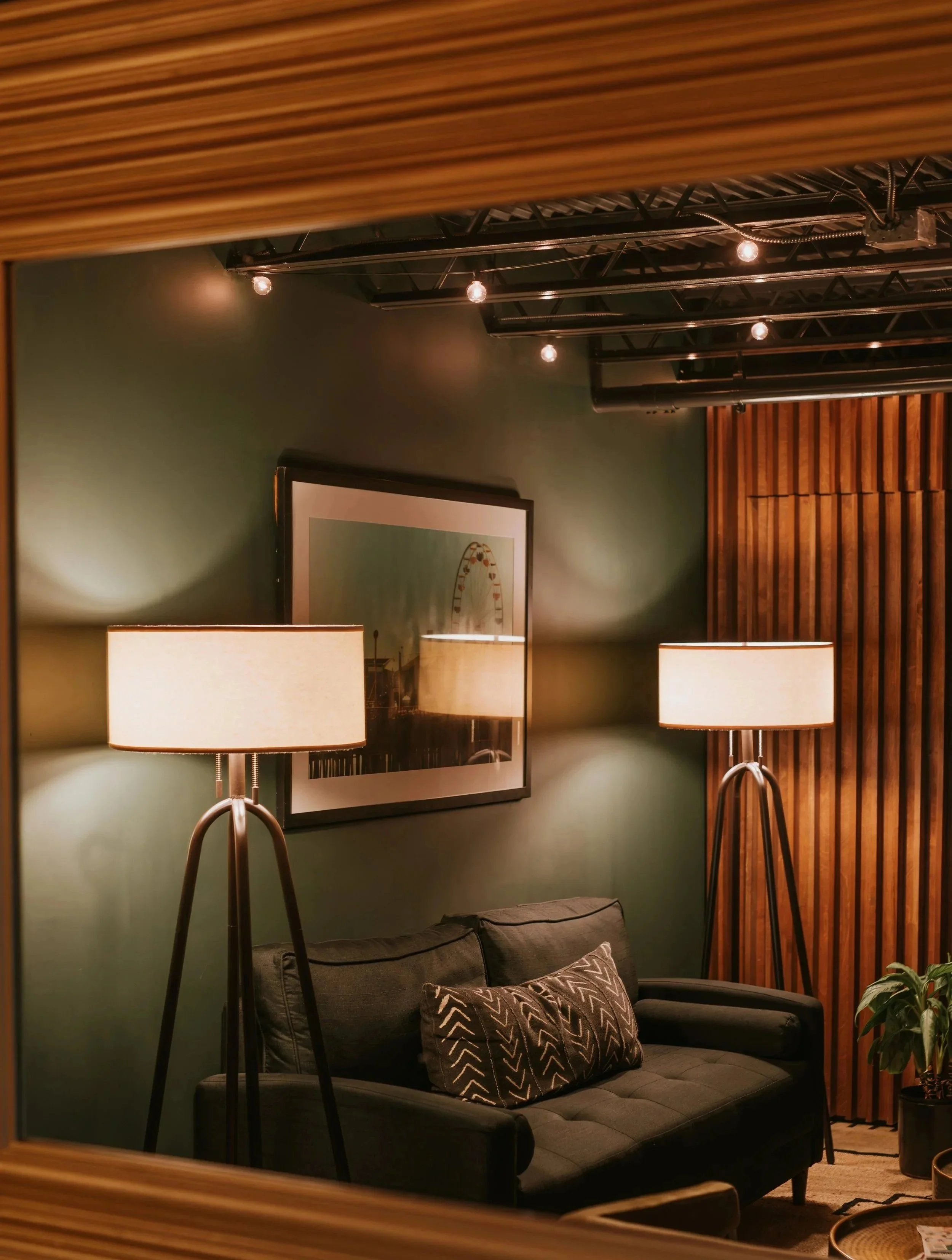 Cozy Green Room corner with a tufted sofa flanked by tripod lamps and framed art