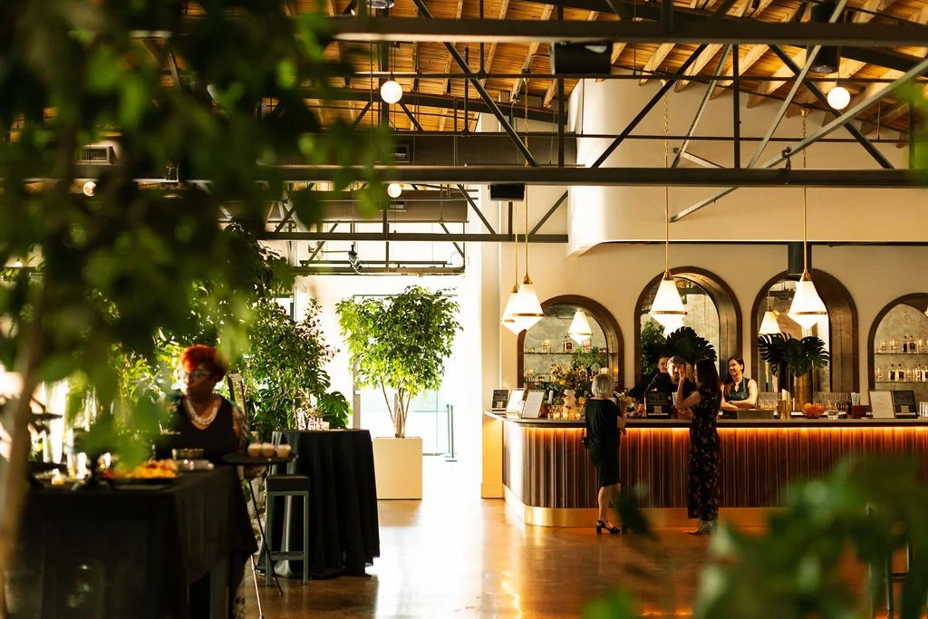 Guests mingling at a warmly lit bar with arched mirrored shelving during a cocktail reception in Saint Elle main space.