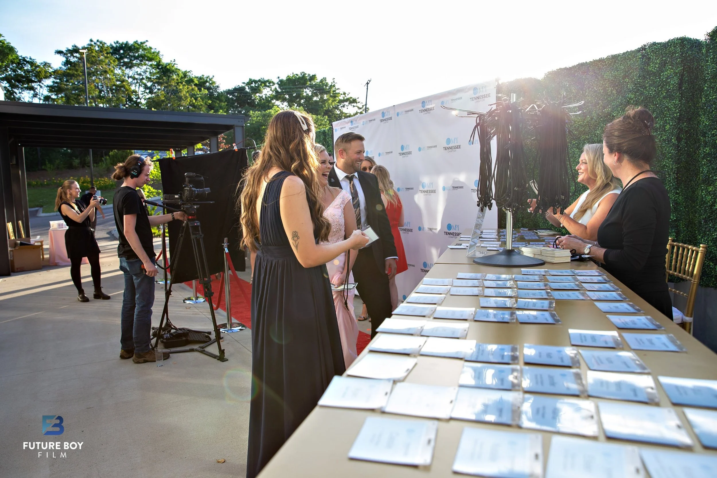 Guests checking in at an outdoor registration table beside a red carpet and step-and-repeat at a corporate event space