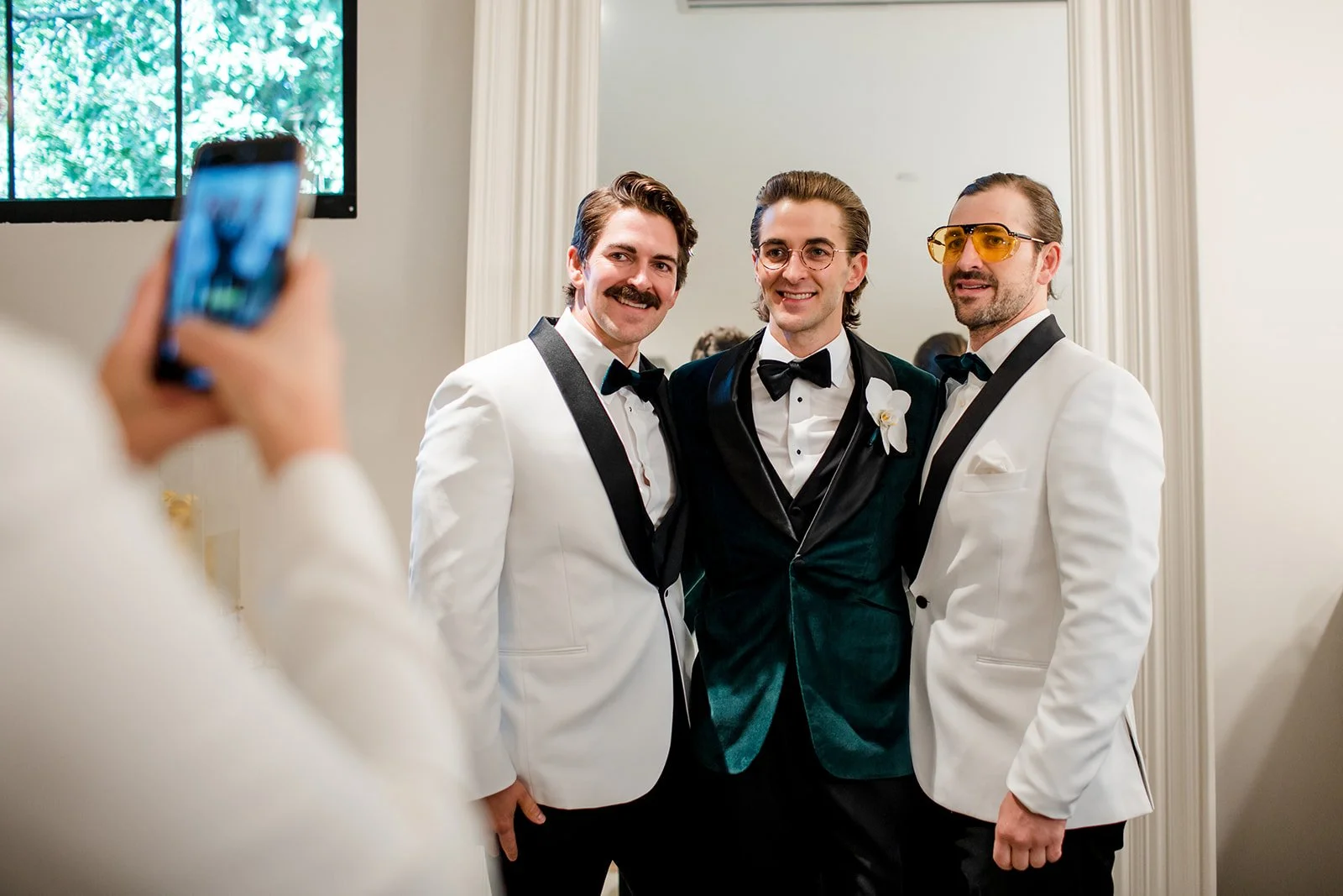 Groom and groomsmen in white and green velvet tuxedo jackets pose for a phone photo